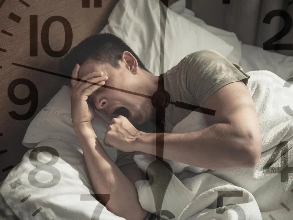 zaburzenia snu; bezsenność; Mężczyzna leży w łóżku, ziewając i zakrywając twarz, z nałożoną tarczą zegara.